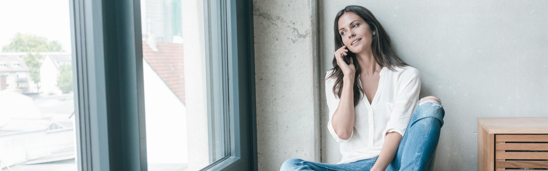 Junge Frau am Handy schaut aus dem Fenster