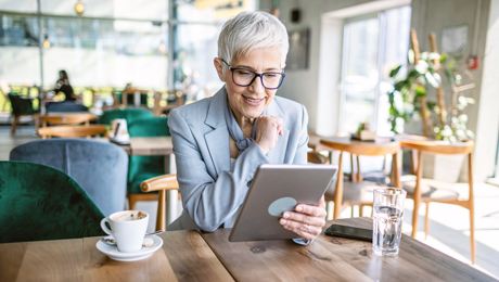 Ältere Frau sitzt mit Laptop im Café