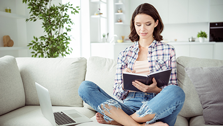 Junge Frau sitzt auf Couch und notiert sich im Notizbuch